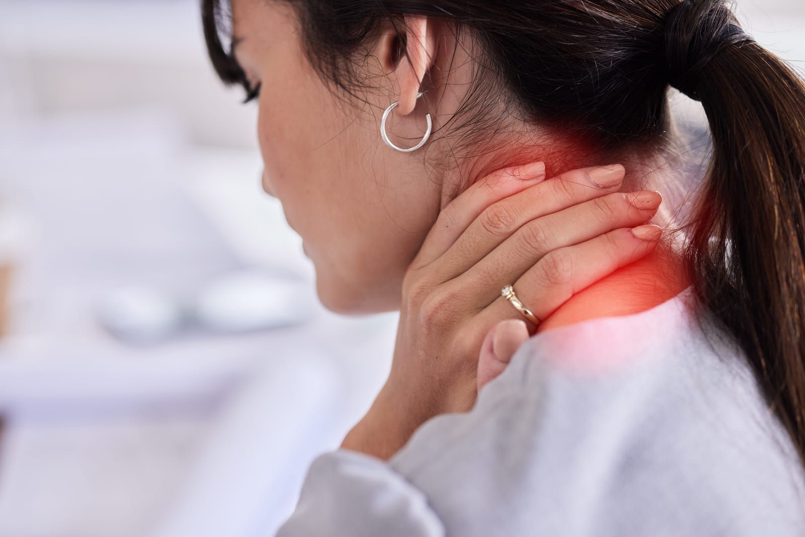 A woman is holding her neck in pain while sitting at a desk.