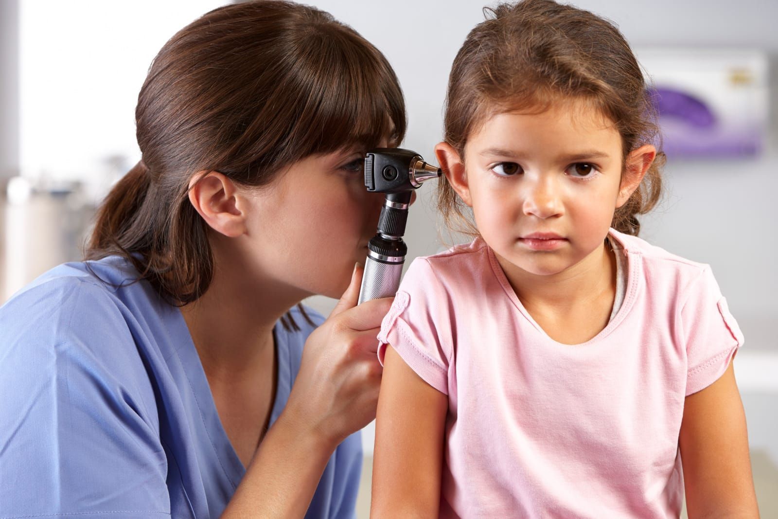 An audiologist examining a little girl 's ear with an otoscope.