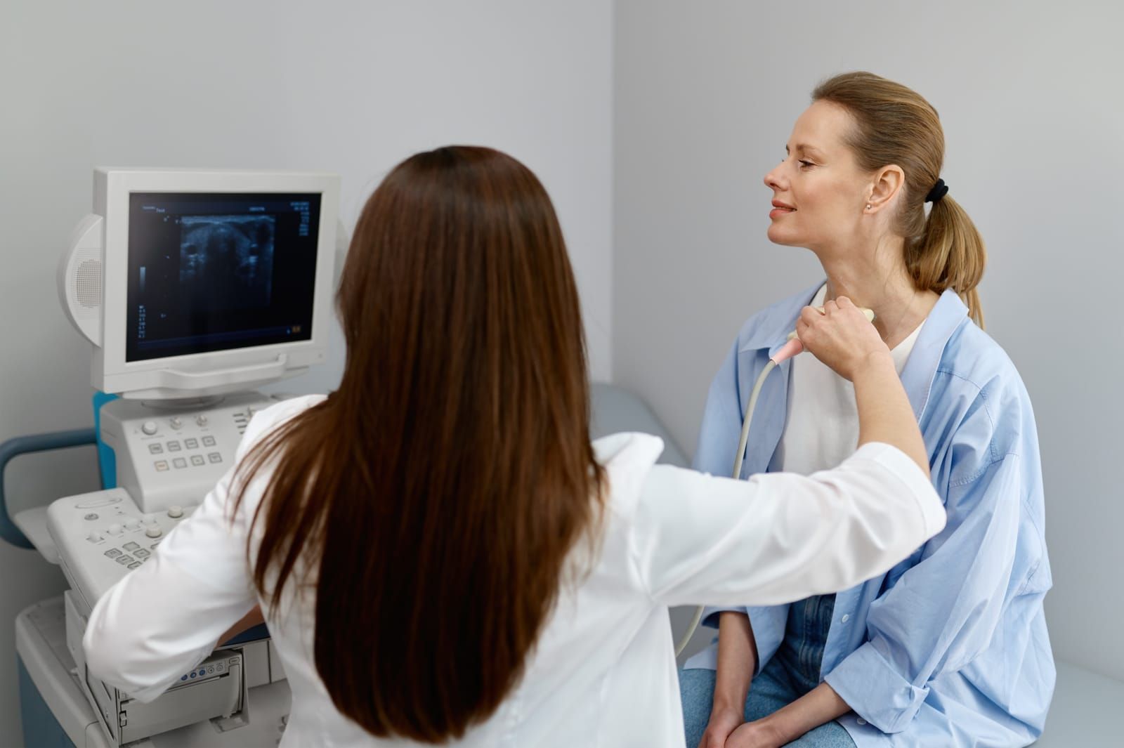 A doctor is examining a patient 's neck with an ultrasound machine.