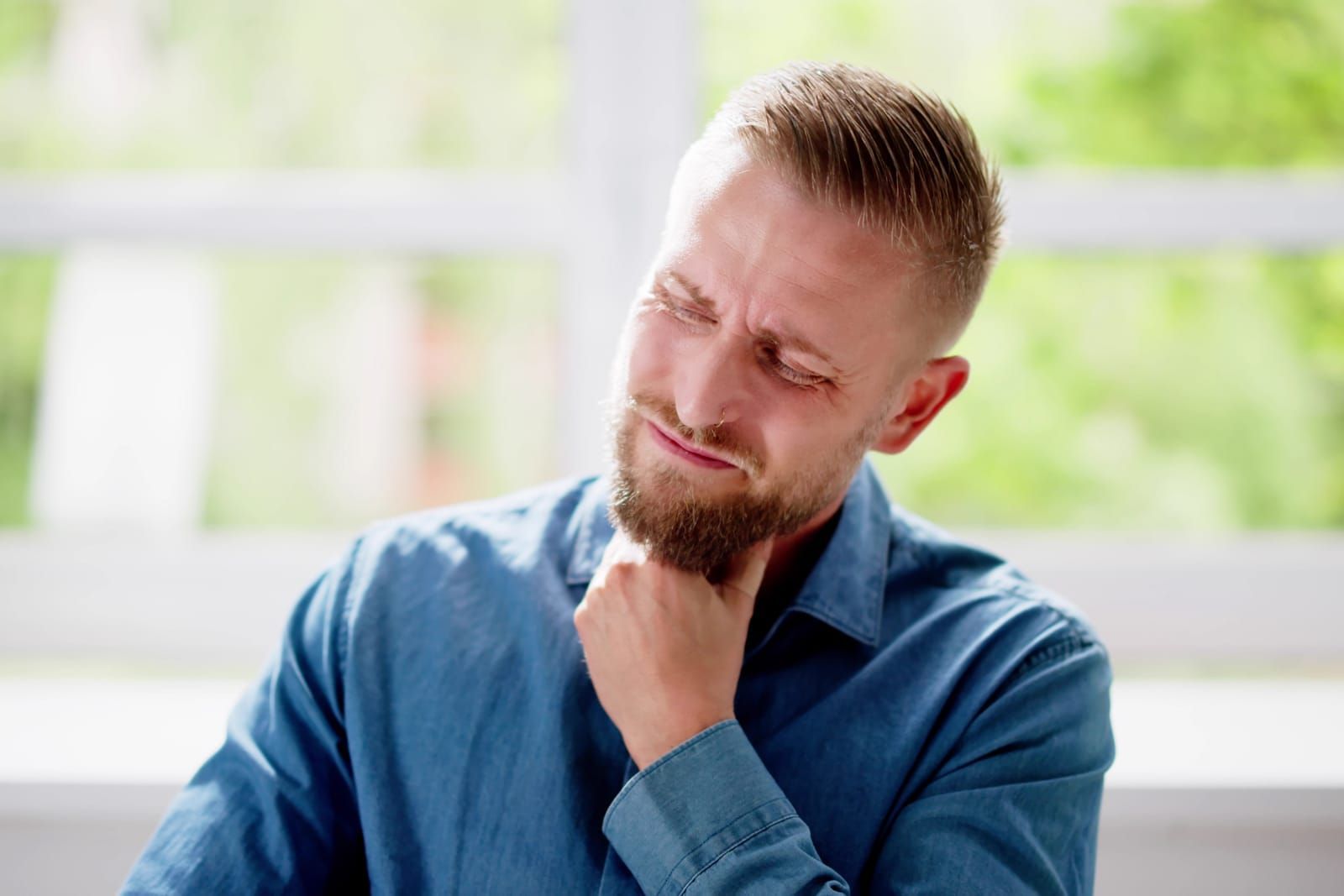 A man with persistent sore throat holding his hand to his chin and looking down.