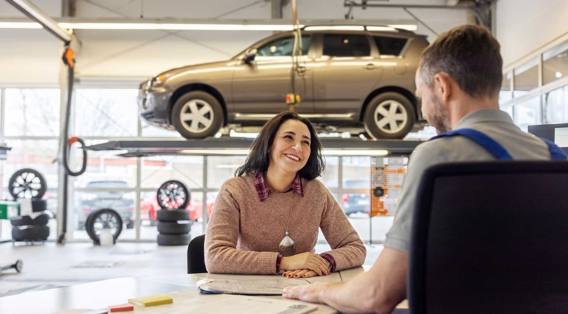 Woman and mechanic discussing car repairs in an auto shop with a car on a lift.
