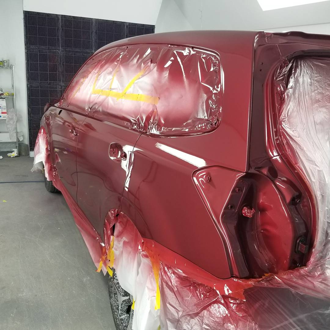 A red car is being painted in a garage