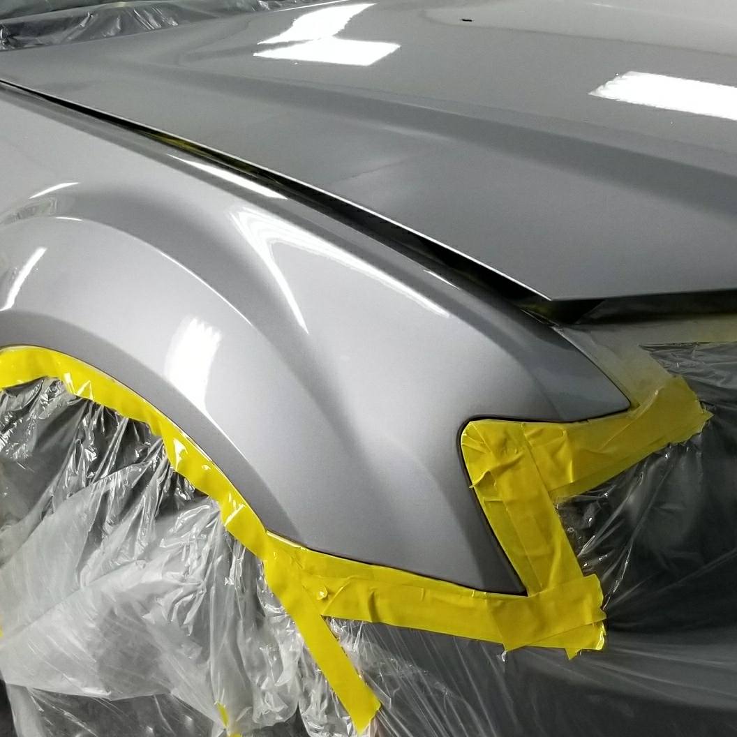 Silver car fender taped for painting.