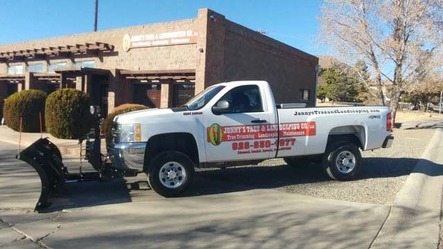 White pickup truck with plow parked in front of a building; signage on truck.