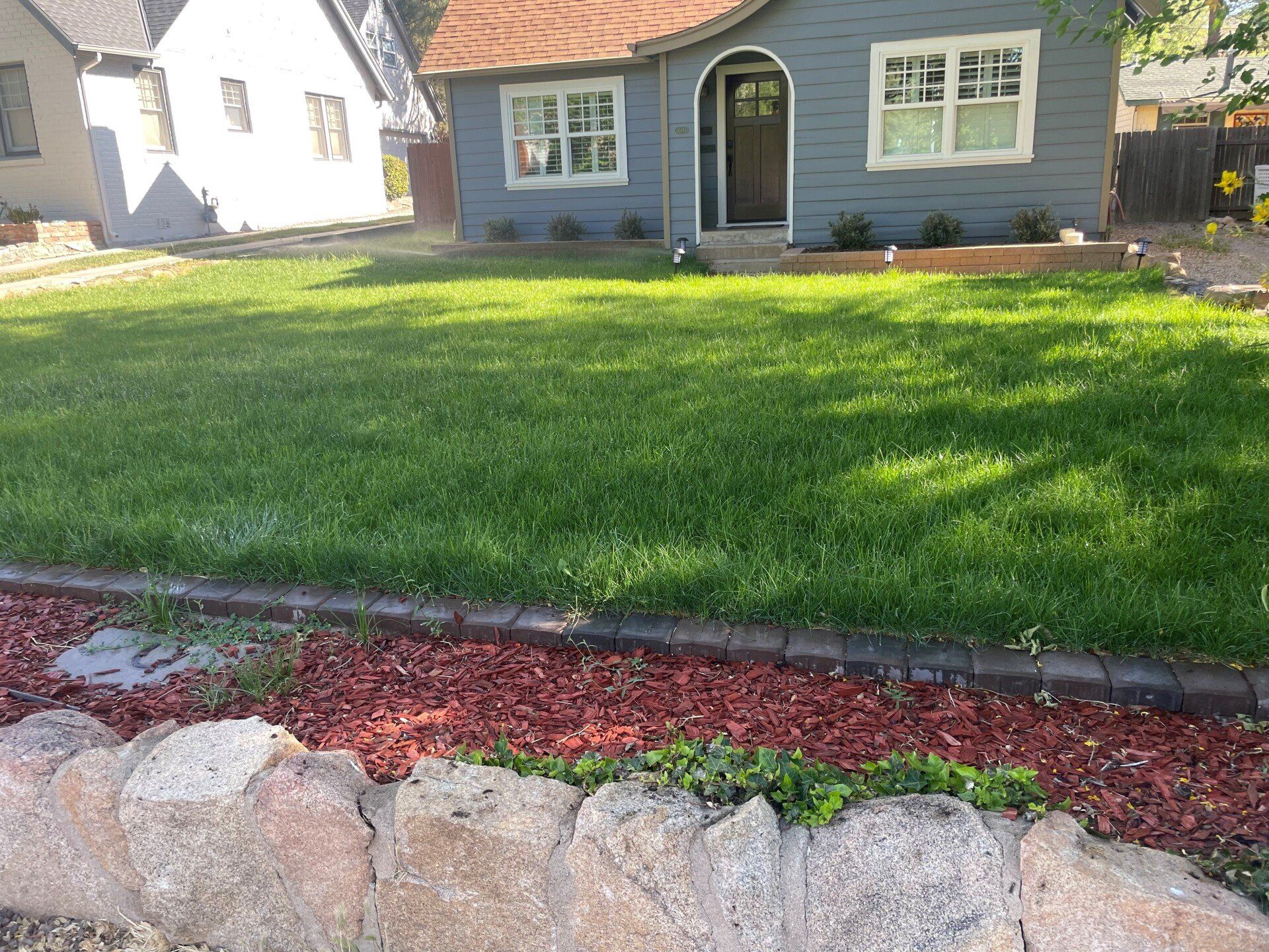 Blue house with a green lawn and a red mulch bed in front.