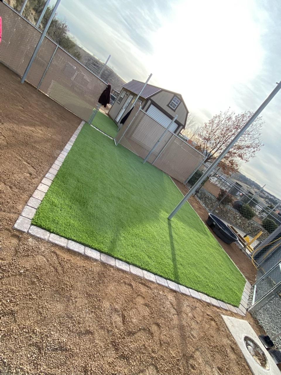 Artificial turf dog run enclosed by fence and bordered with stone pavers.