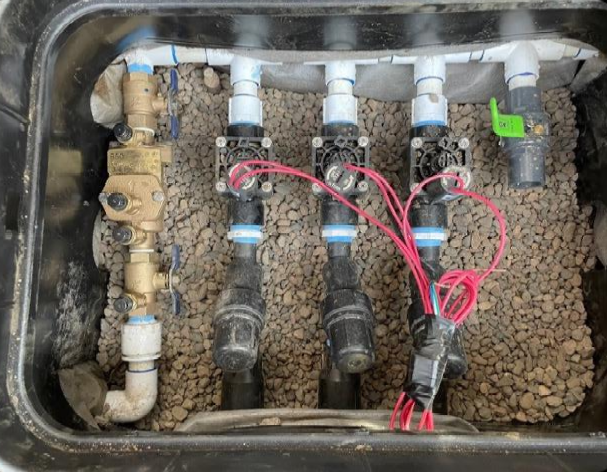 Irrigation valve box with water lines, valves, and electrical wiring on top of gravel.