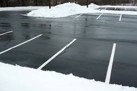 Wet, empty parking lot with white parking lines, partially covered with snow.