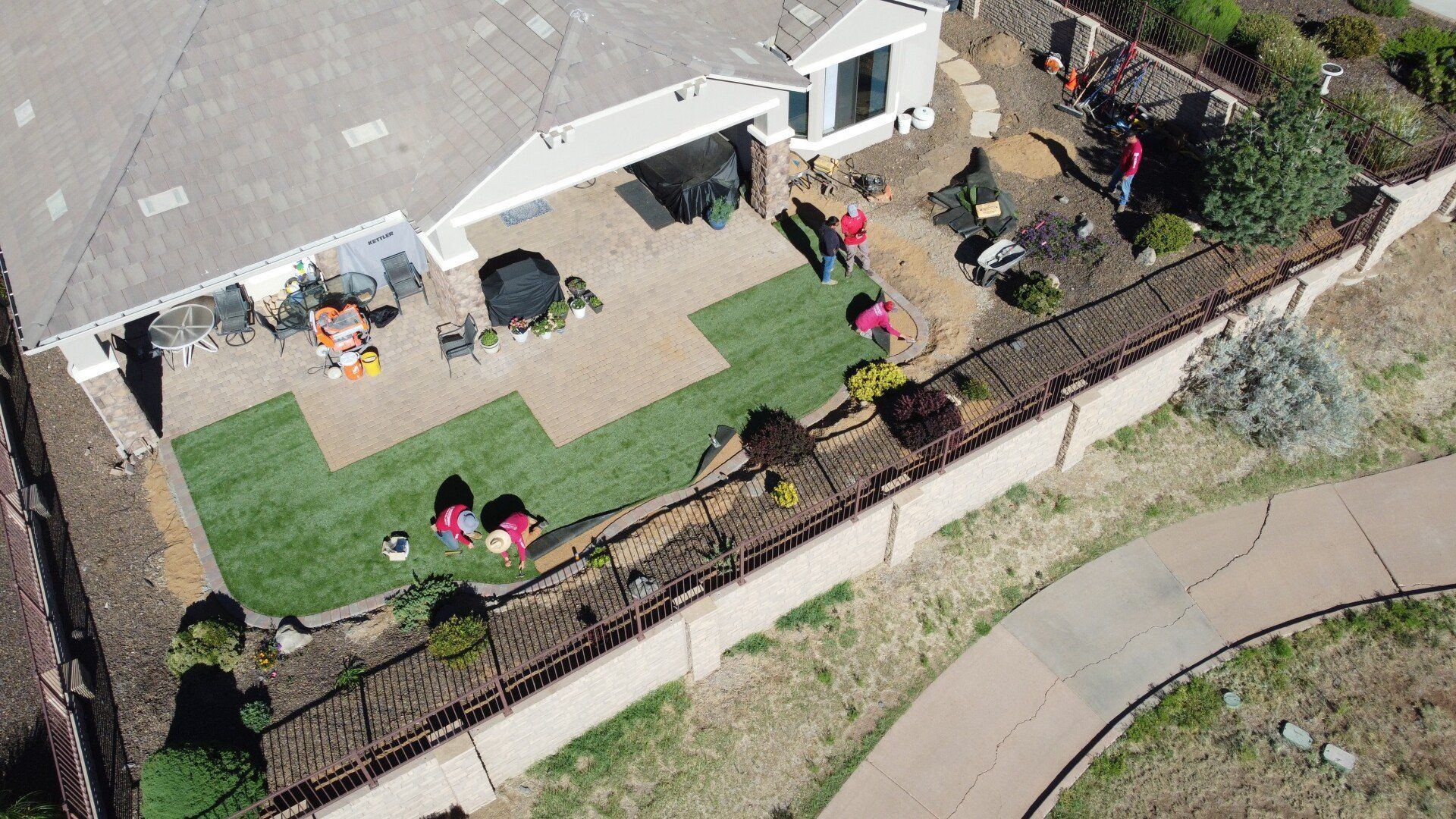 Aerial view of a yard with brick patio, green grass, and workers near a house.