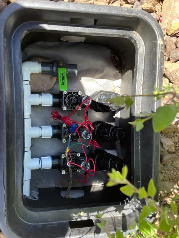 Irrigation system control valves inside a black box, with white PVC pipes and electrical wiring.