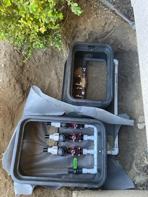 Open irrigation valve boxes in dirt. Valves and piping are visible.