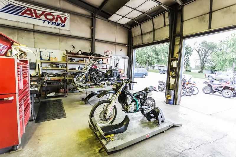 Motorcycle repair shop with bikes on lifts, tools, and open garage door.