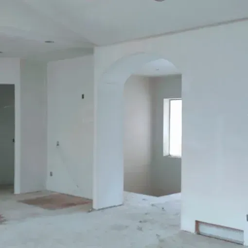 Empty interior of a room under construction, featuring white walls, arched doorway, and a window.