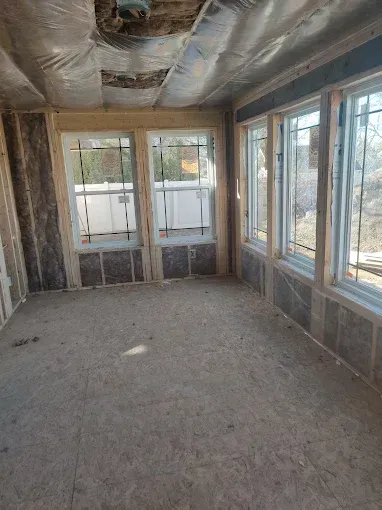 Interior of a room under construction with windows and exposed framing and insulation.