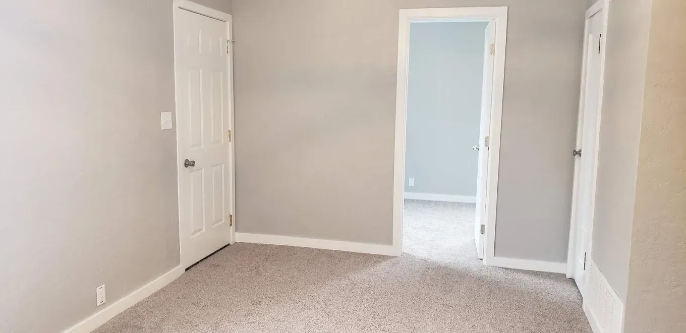 Empty room with carpet, grey walls, and white doors.