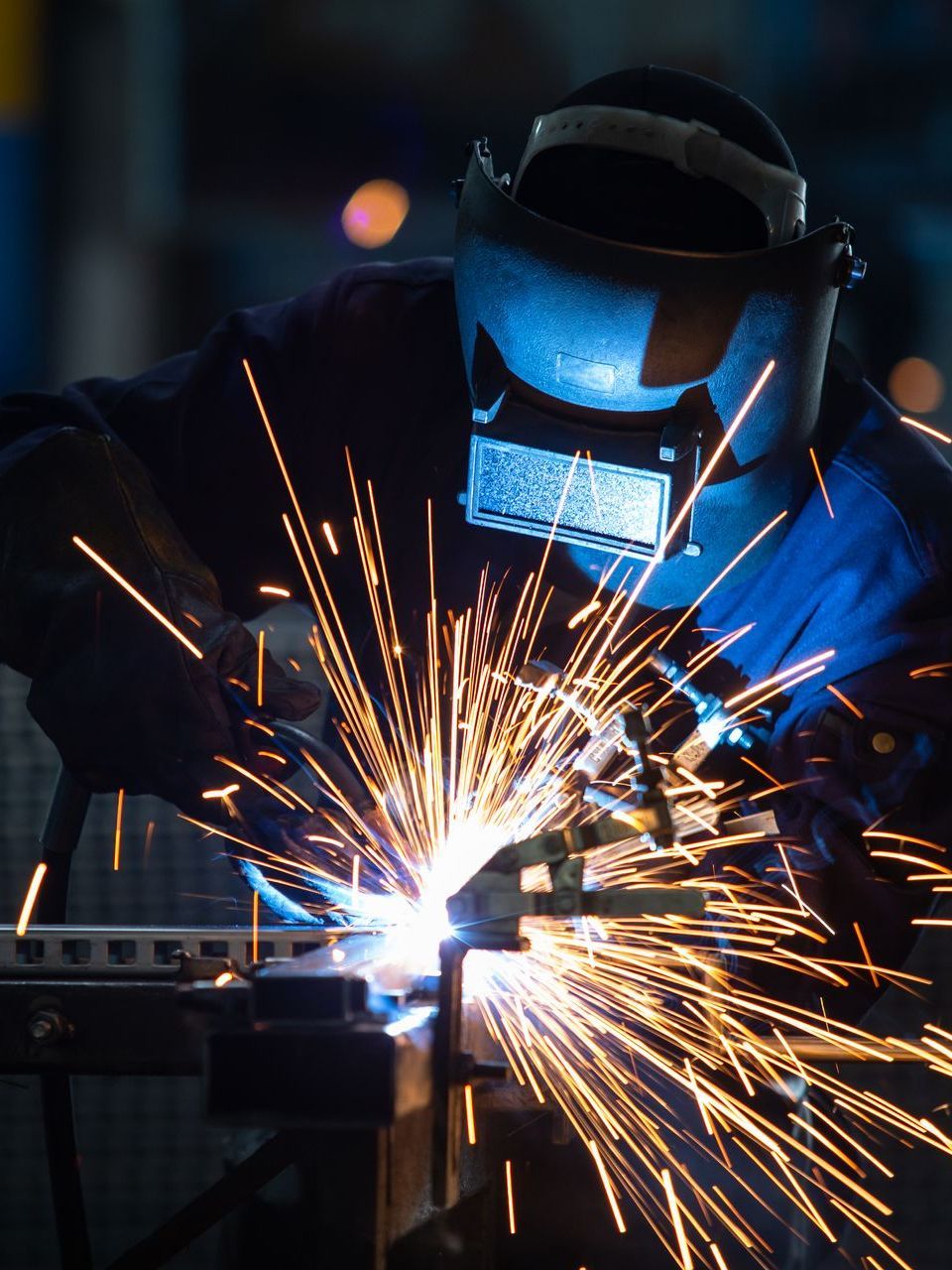 A man wearing a welding mask is welding a piece of metal.