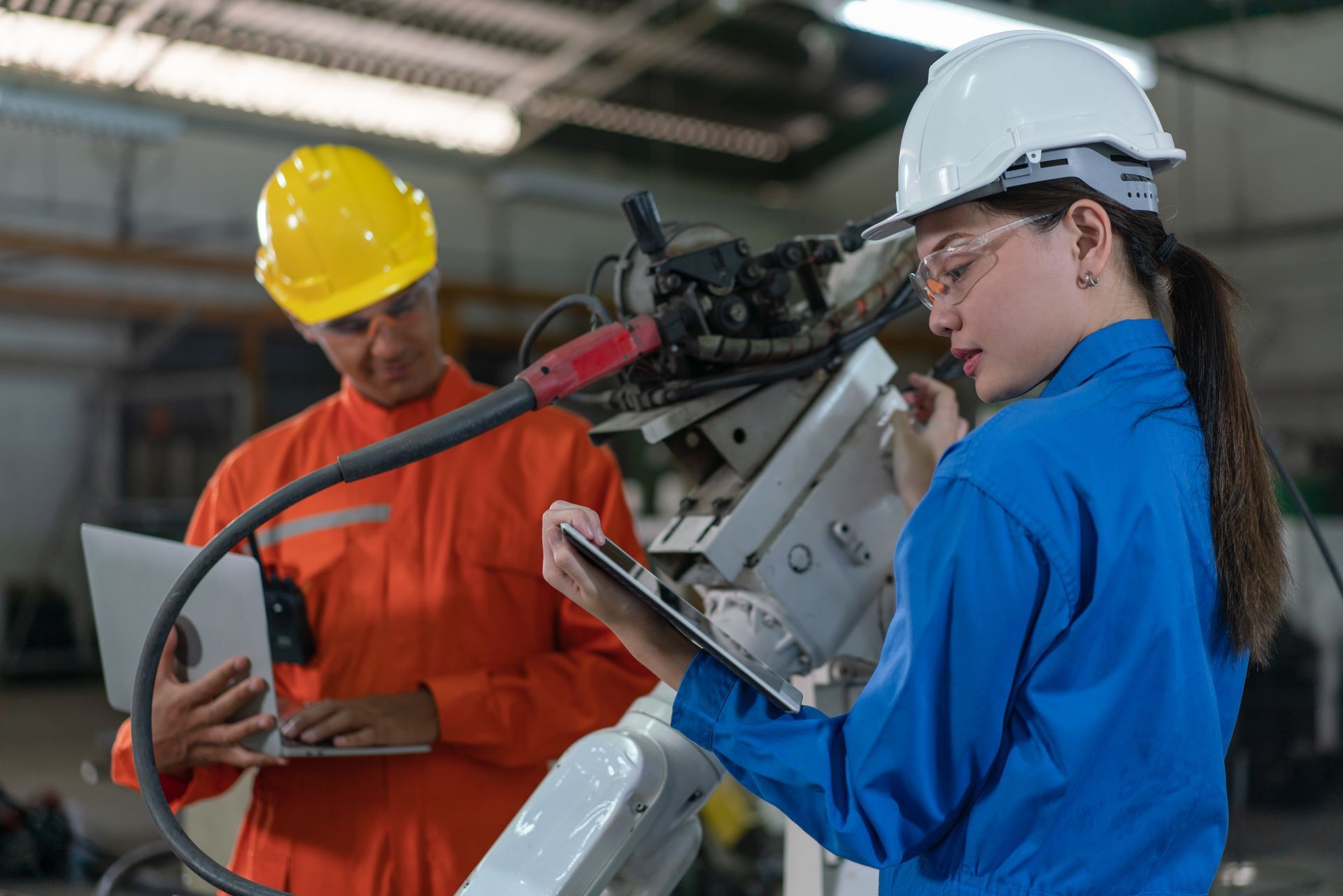 A man and a woman are working on a robotic arm in a factory.