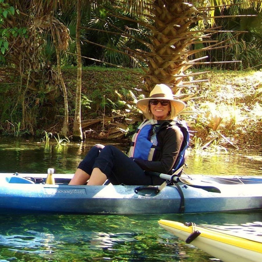 Woman in a kayak, wearing a hat and life vest, paddling on a clear river.
