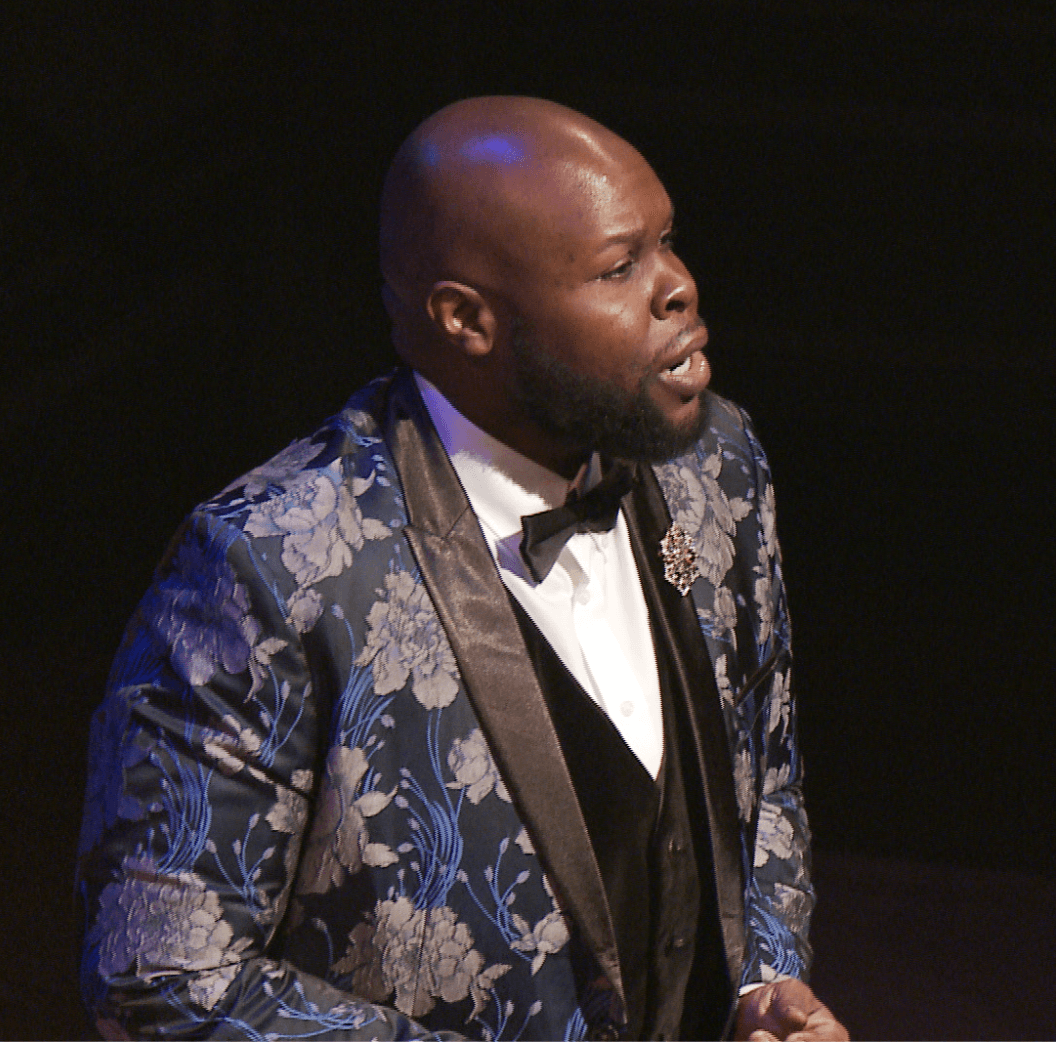 Man in a blue floral tuxedo, singing on stage.