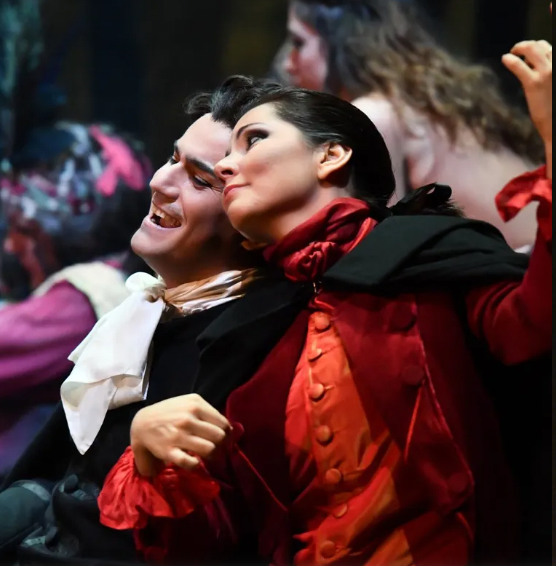 Actors in period costumes, man laughing, woman looking up, rich reds and black.