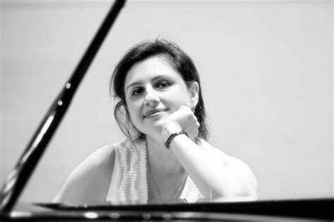 Woman at a piano, resting chin on hand, smiling. Black and white photo.