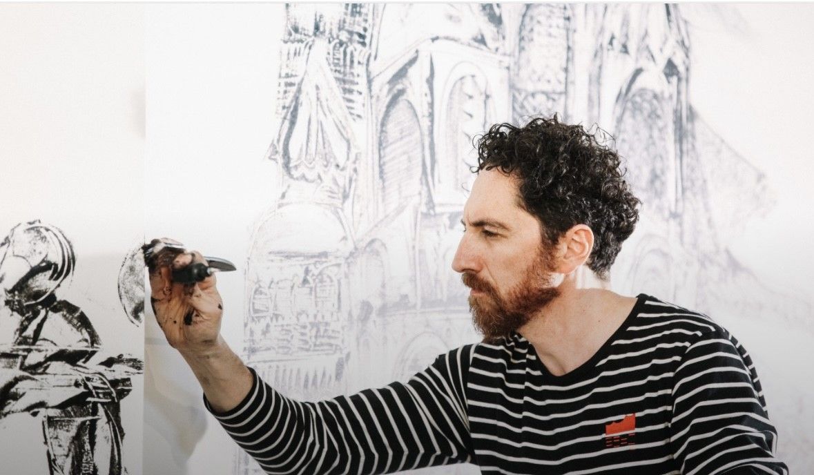 Man with beard painting a large, grayscale architectural drawing on a white wall.