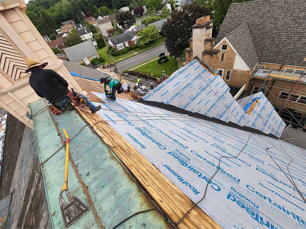 Woman in straw hat smiles, holding wine glass near a lake.