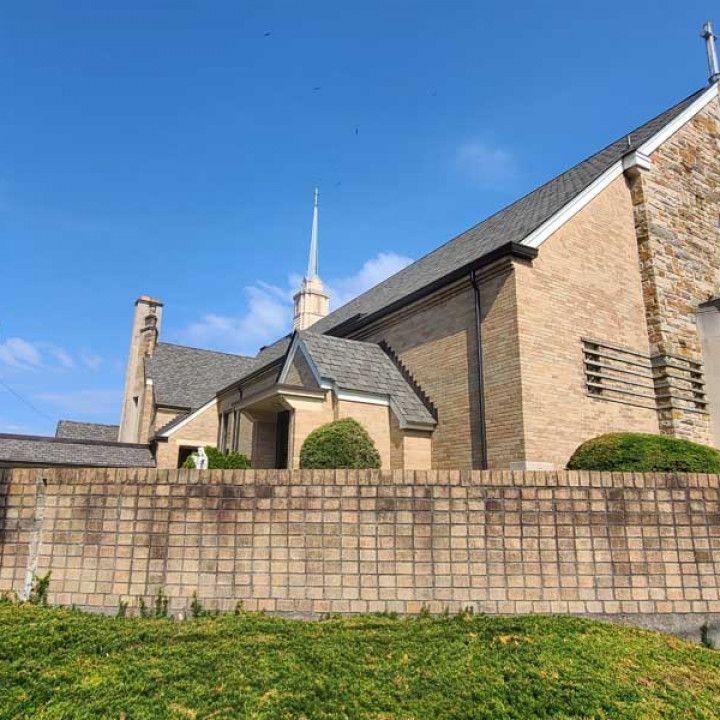 Woman in straw hat smiles, holding wine glass near a lake.