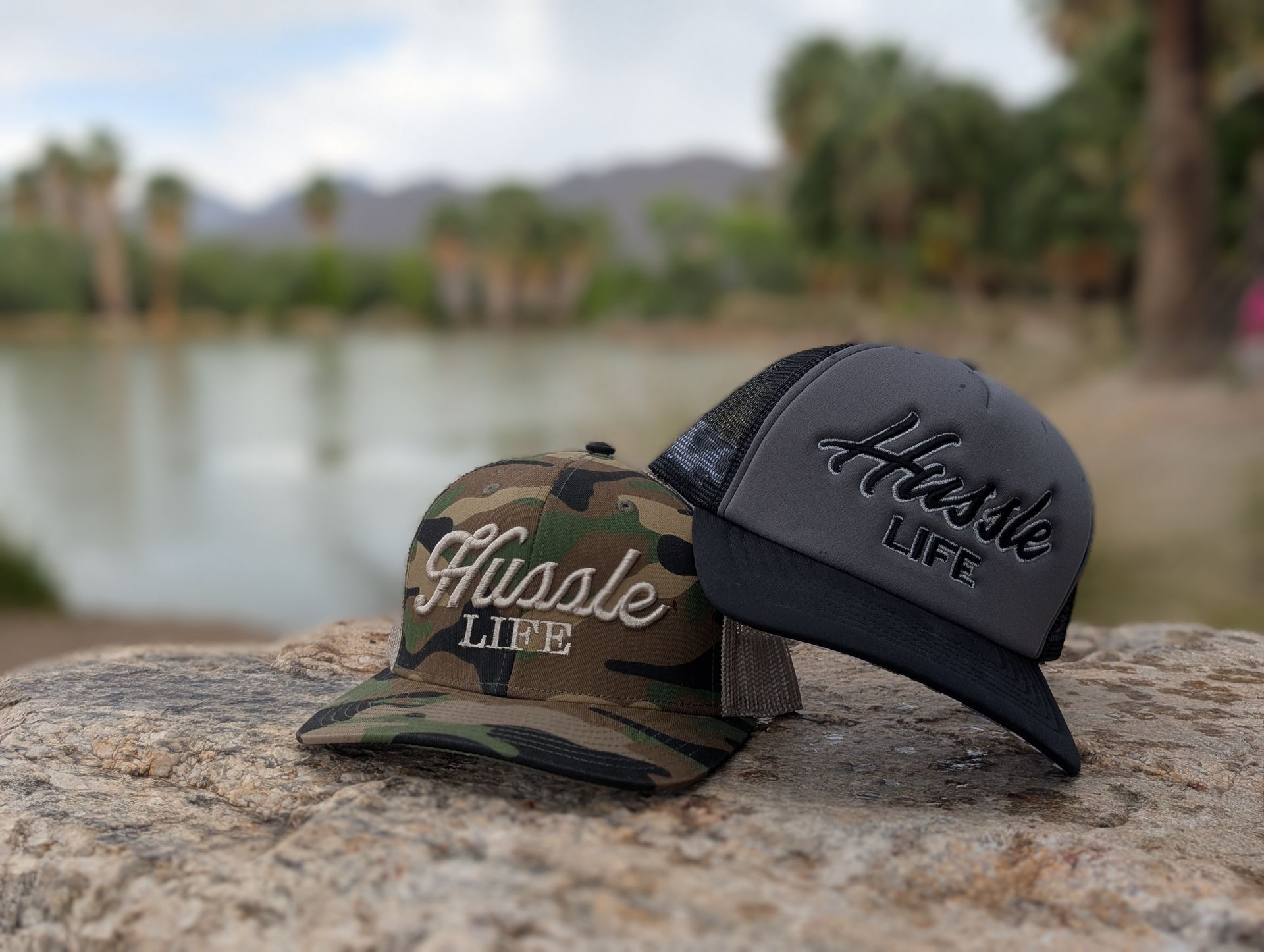 Two hats are sitting on a rock in front of a body of water.