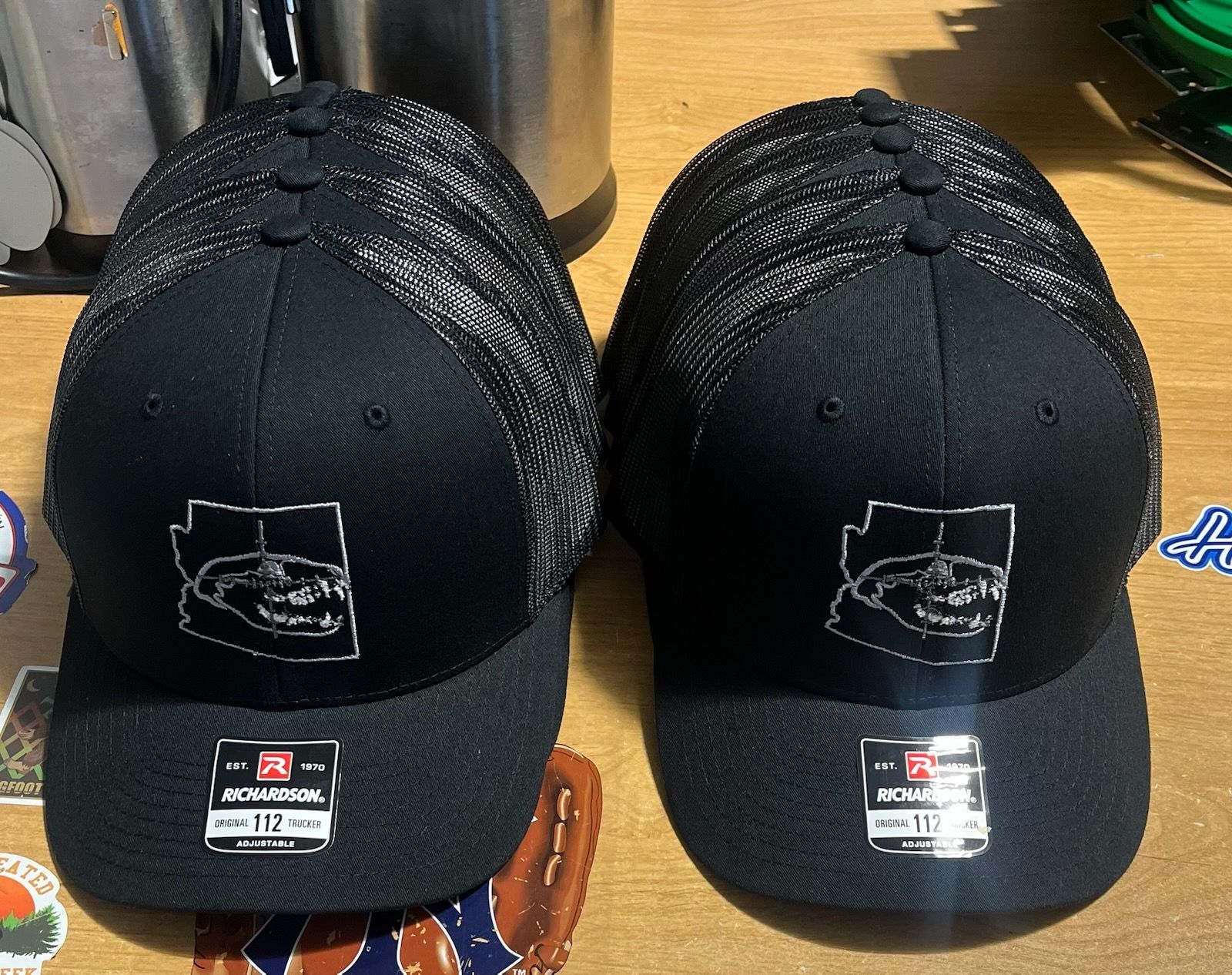 Two black caps with white logos and mesh tops; side-by-side on a wooden surface.