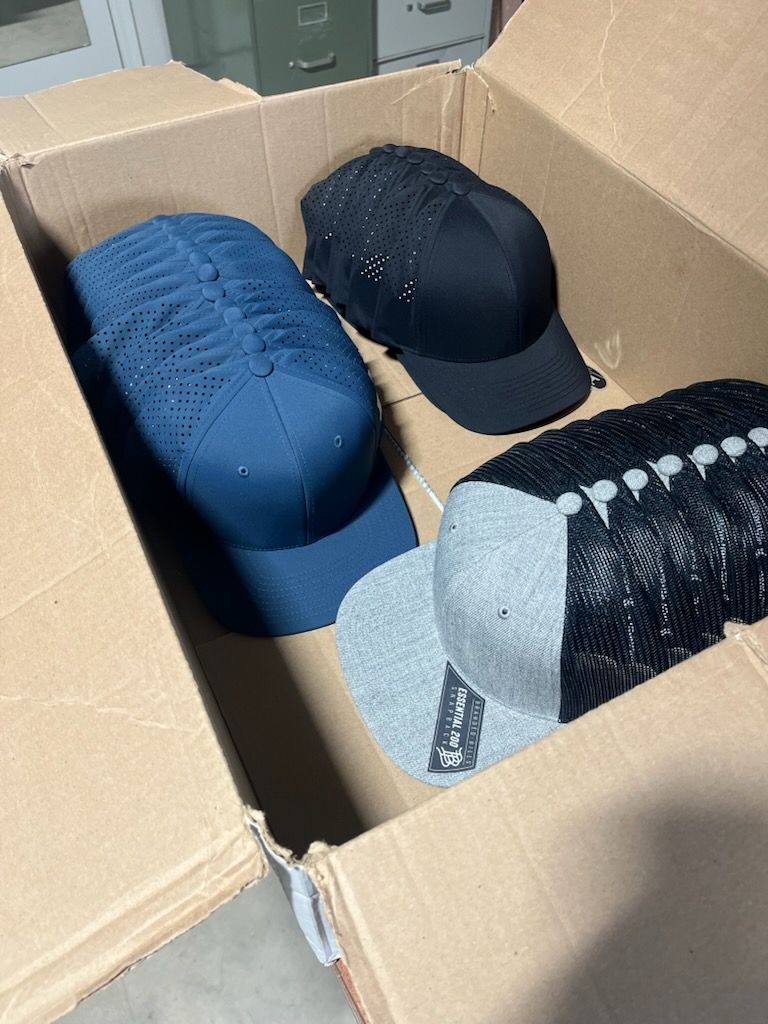 Cardboard box filled with four hats: blue, black, and gray, packed for shipping.