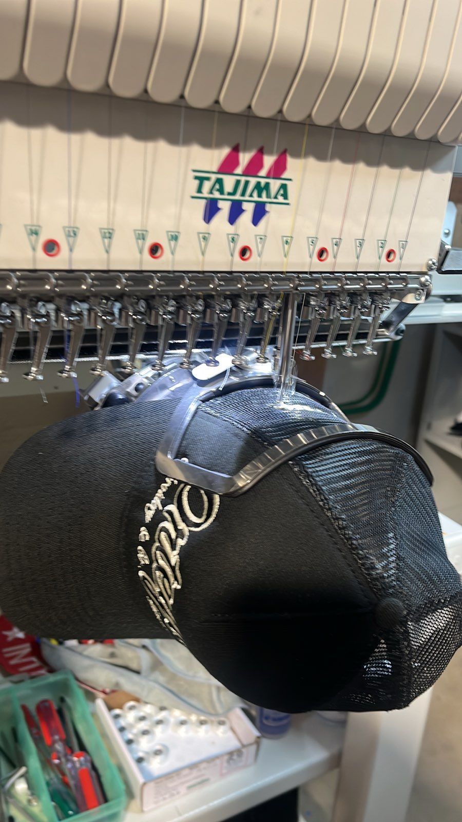 An embroidery machine stitching a design on a black hat.
