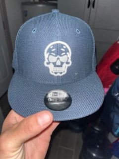 Blue baseball cap with white skull logo, held by hand.