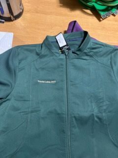 Green jacket with a tag, lying on a wooden surface.