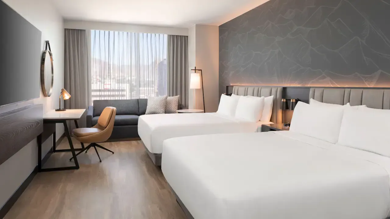 A grey and white hotel room with hardwood floors and two beds , a couch , a desk and a chair.