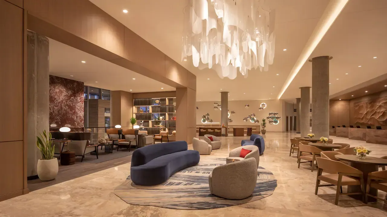 A hotel lobby with a couch , chairs , tables and a chandelier.
