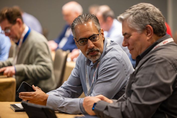 Two men in a conference setting looking at a mobile phone. 