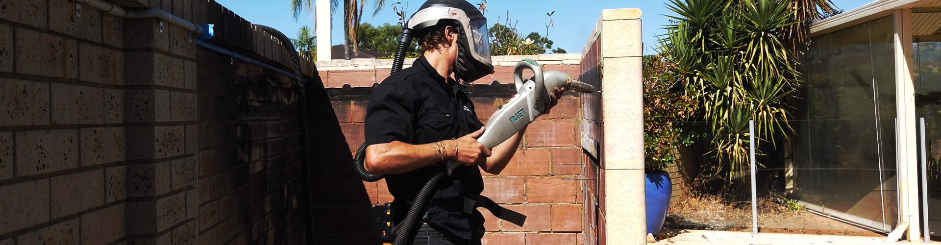 A man wearing a helmet is using a drill on a brick wall.