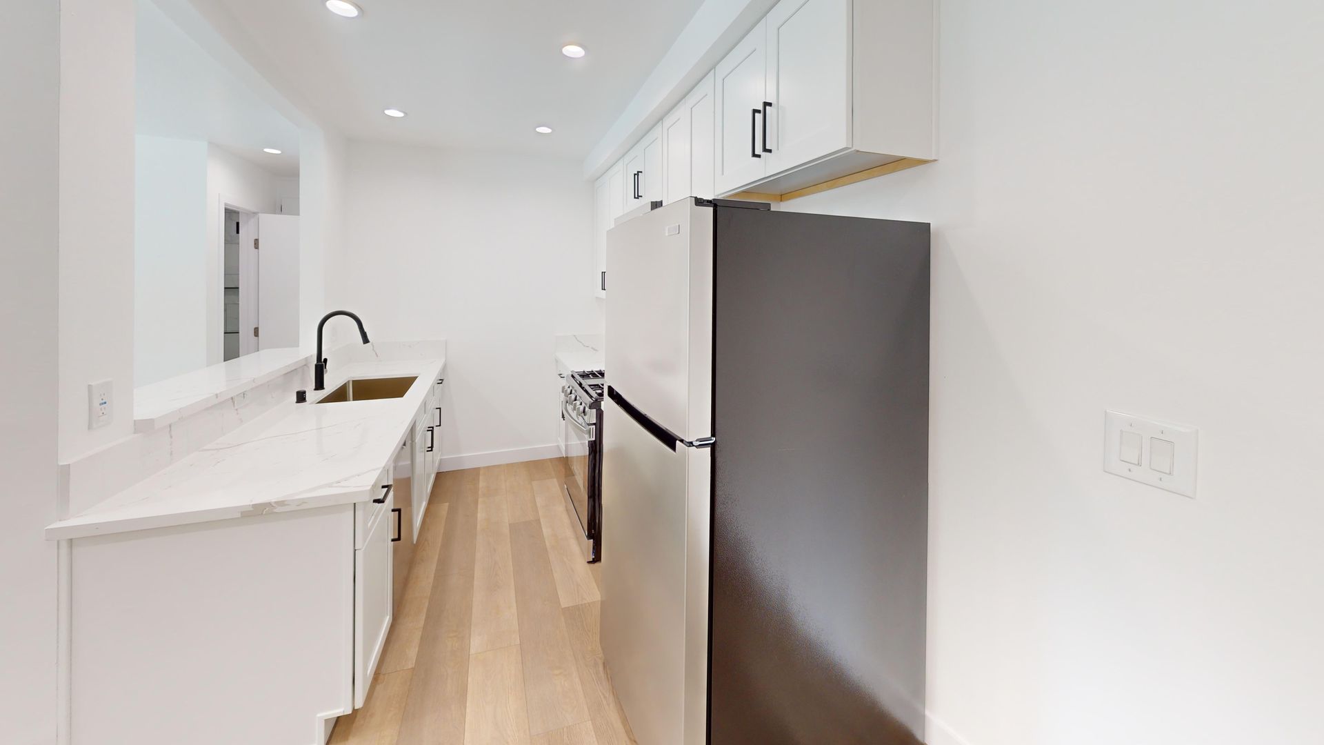 Bright, modern kitchen with white cabinets, stainless steel appliances, and wood flooring.