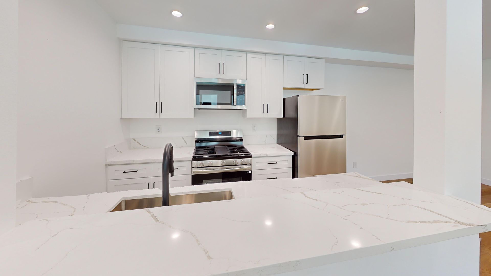 Modern white kitchen with stainless steel appliances, marble countertops, and a sink.