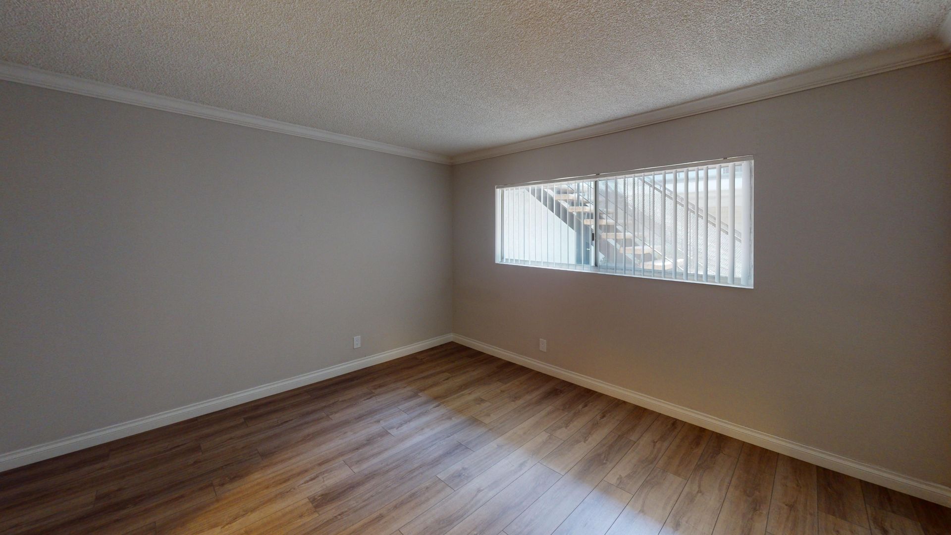 Empty room with wood-look flooring, light gray walls, white trim and ceiling, and a window with blinds.