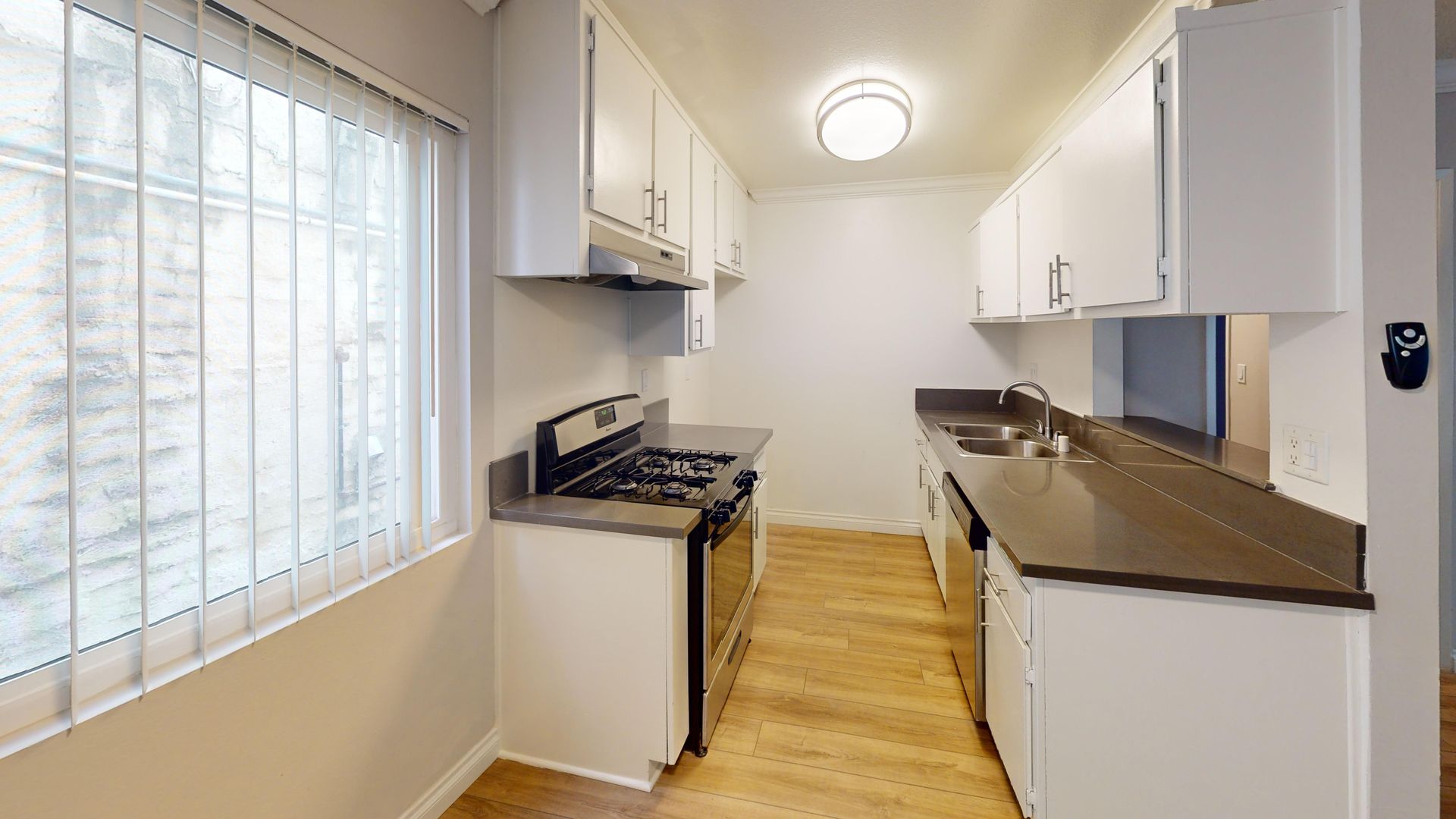 Narrow kitchen with white cabinets, dark countertops, and a stove. A window is on the left.
