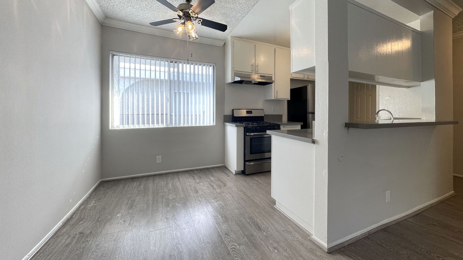 Interior view of a kitchen and dining area with hardwood floors, a stainless steel stove, and a window with blinds.
