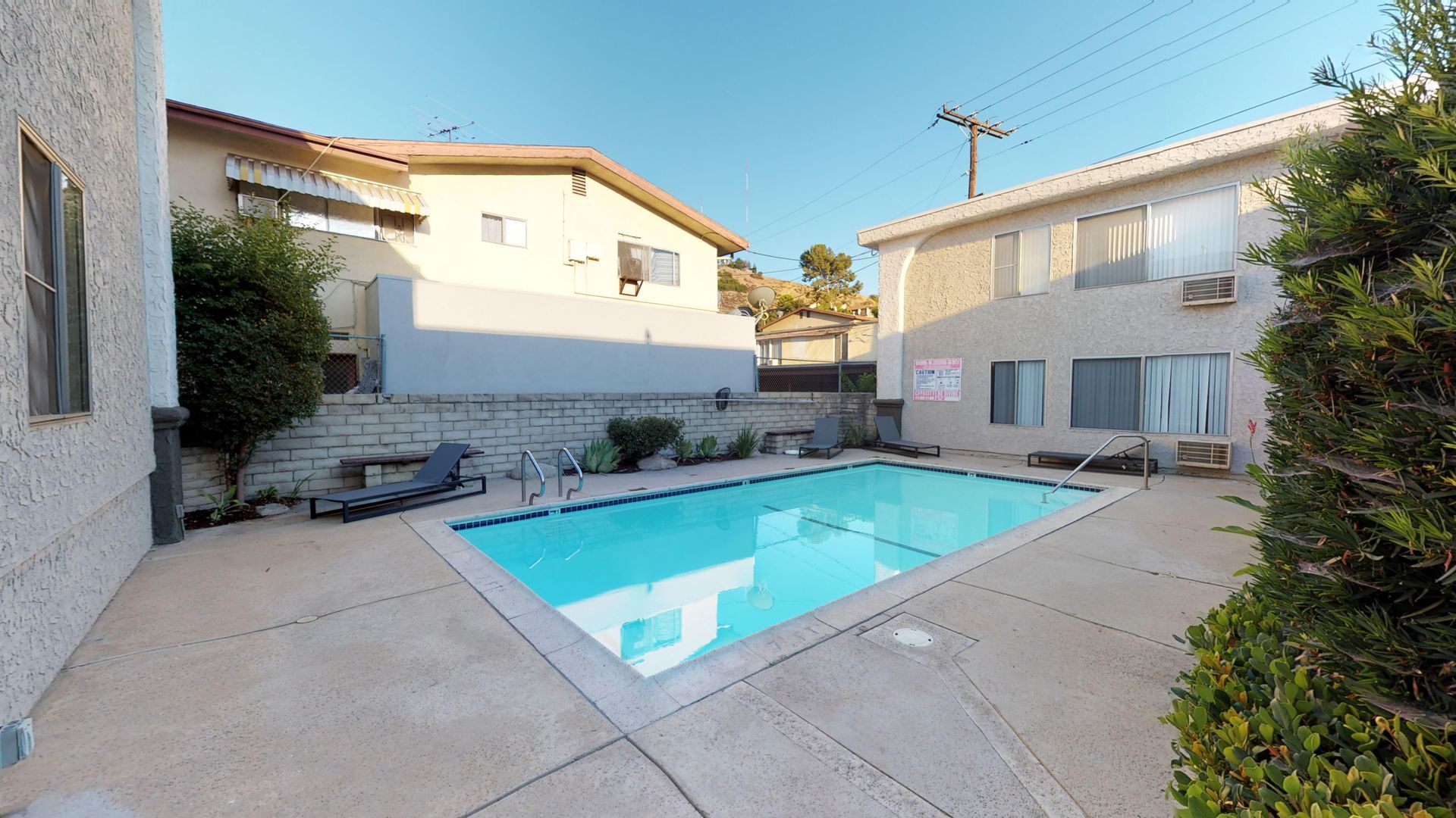 Pool surrounded by buildings. Blue water reflects sky. Concrete patio.