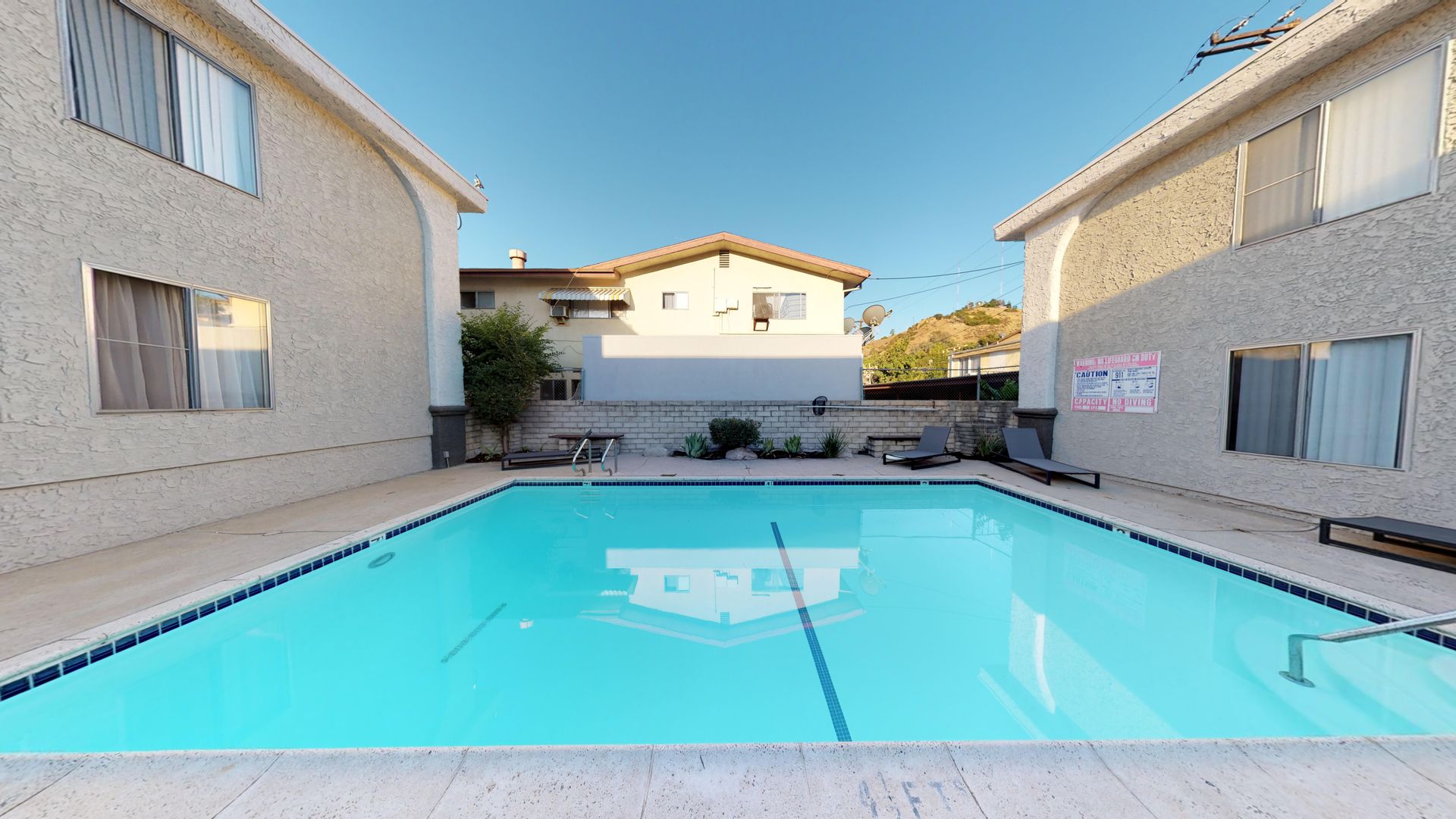 Swimming pool between two apartment buildings under a blue sky.