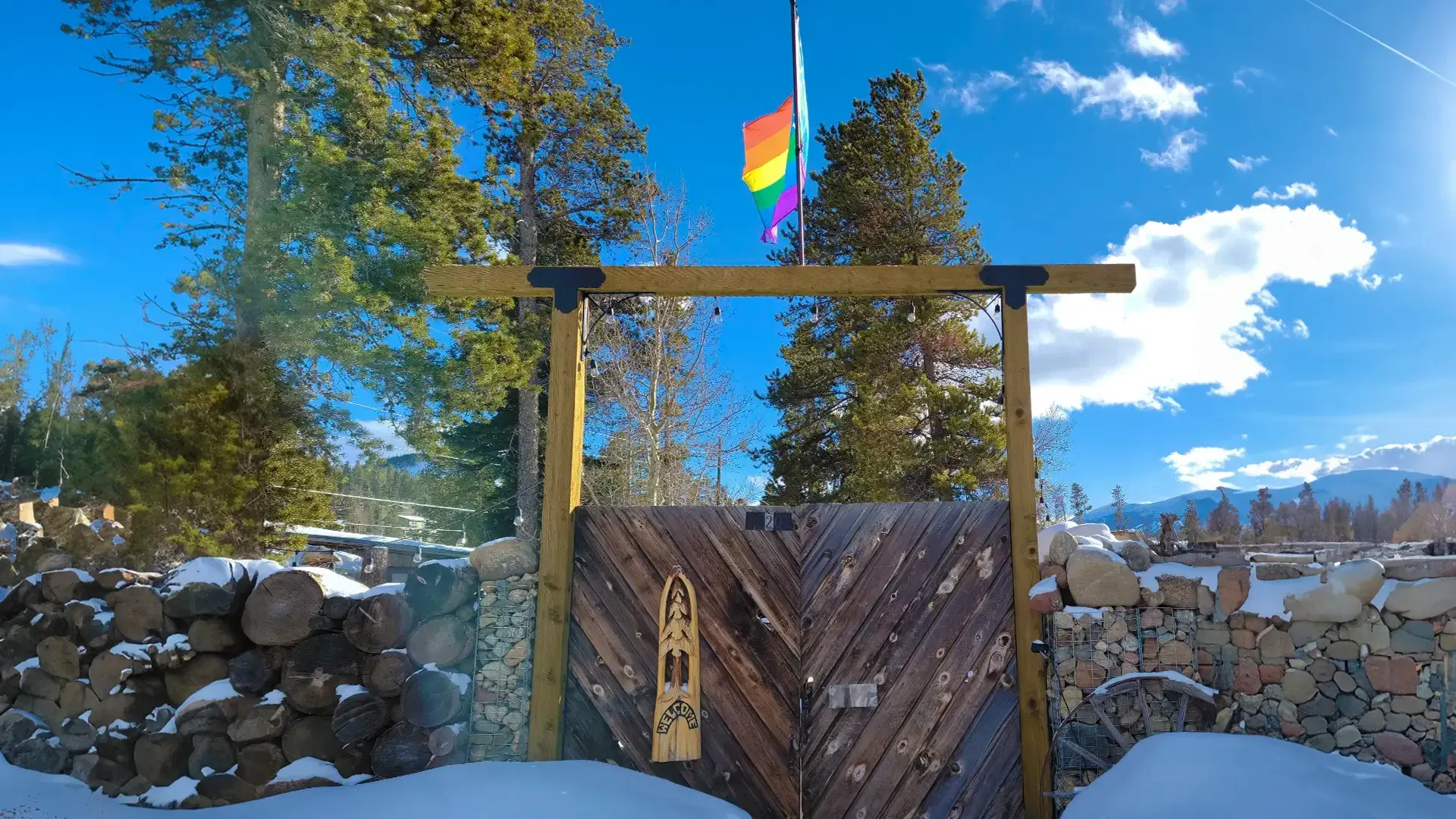 A rainbow flag is flying over a wooden gate in the snow.