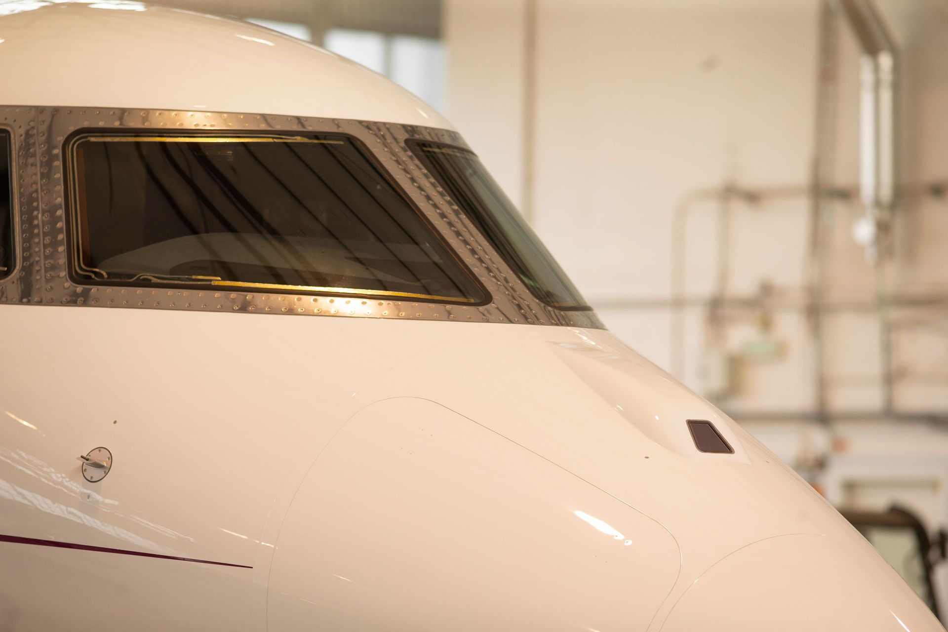Front of a white jet aircraft with cockpit windows in a hangar
