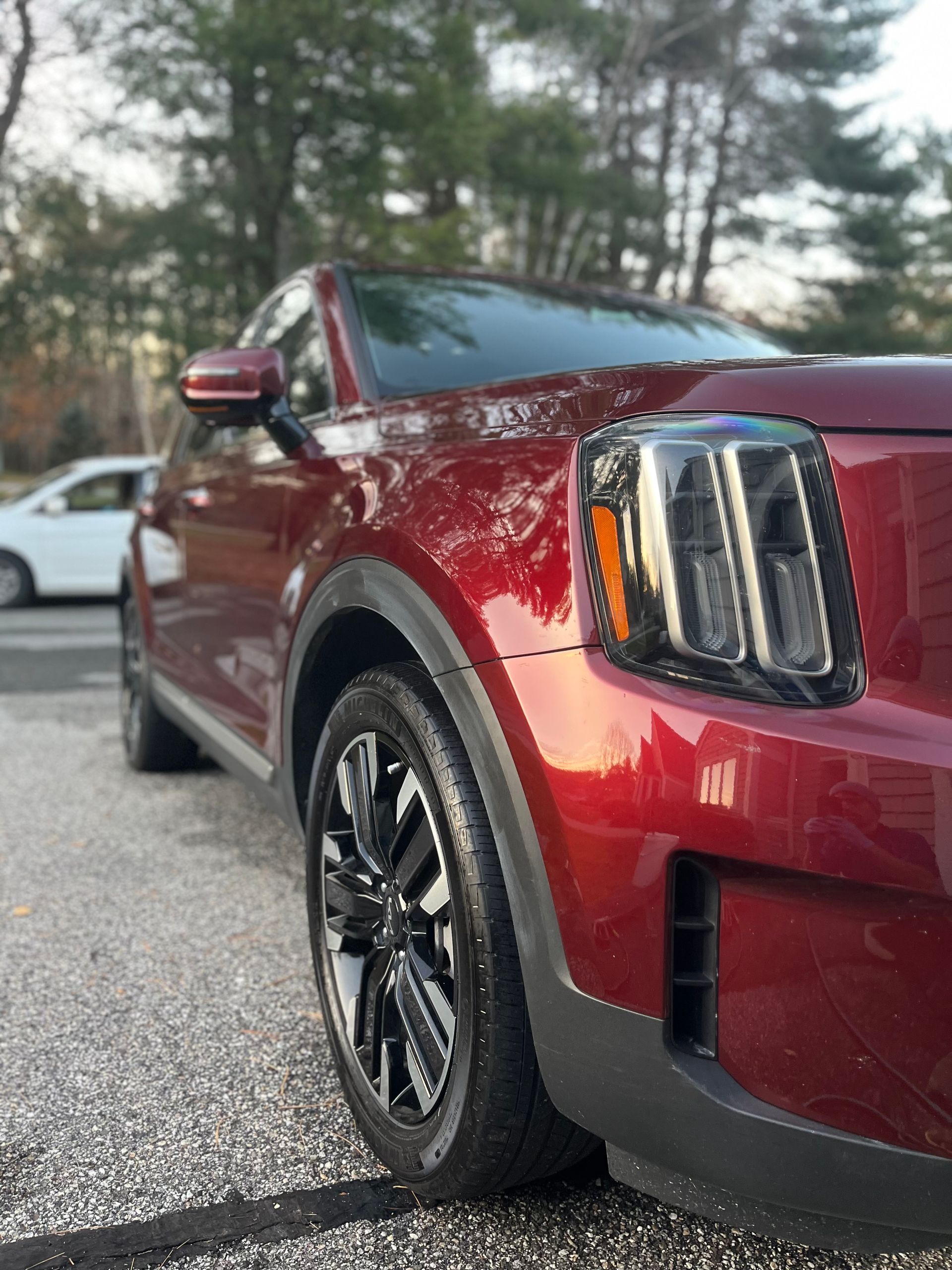 Red SUV parked outdoors, close-up of front headlight and wheel.