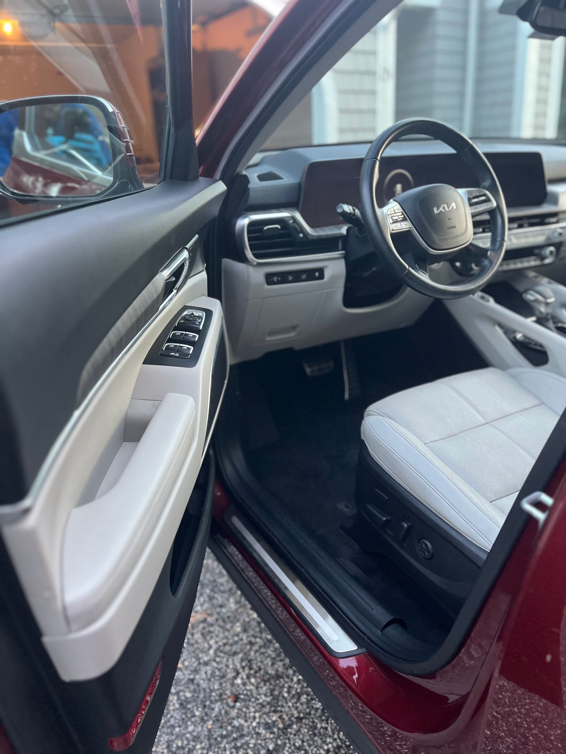Car interior with open driver door, black-and-white seats, and maroon exterior visible.