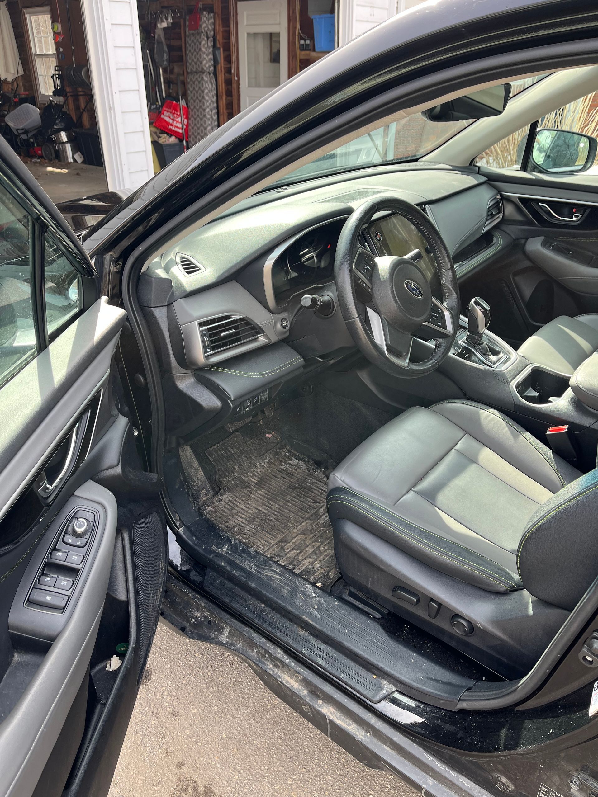 Open car door showing black leather driver’s seat and dashboard interior.